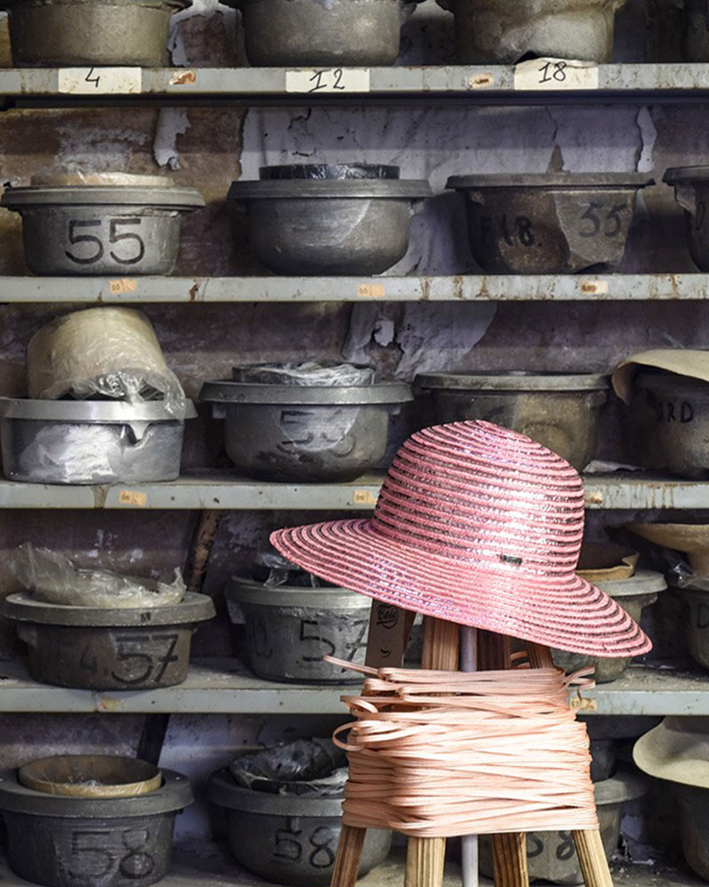 Cappello di Panama Originale : Cappello Tesi di colore rosa appoggiato su un piedistallo, davanti ad una fila di stampi per cappelli